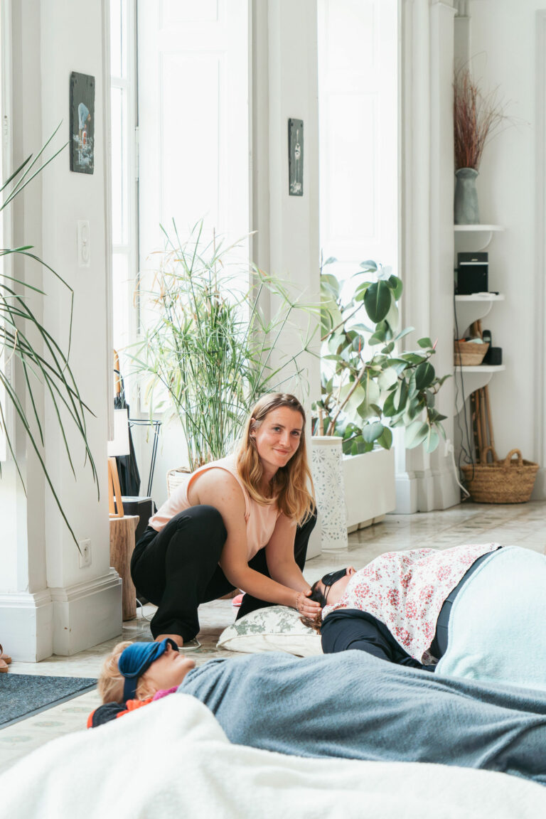 Une jeune femme est accroupie au dessus d'une personne qui elle est allongée, elle lui donne du reiki, un soin énergétique grâce à ses mains.